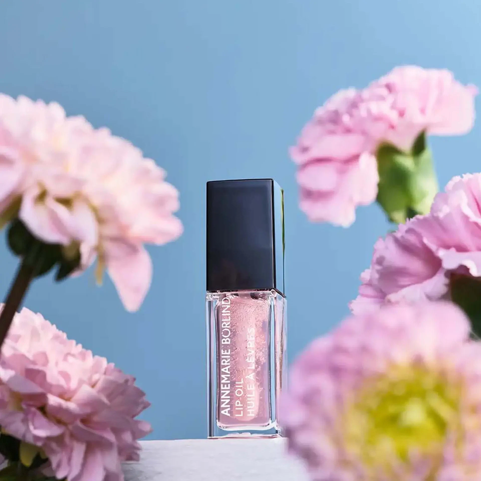 LIP OIL Cherry Blossom von ANNEMARIE BÖRLIND vor blauem Himmel, umrahmt von rosa Blüten
