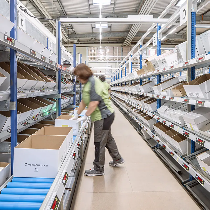 Mitarbeitende in der Logistik von BÖRLIND kommissioniert Produkte an einer modernen Förder- und Regalanlage