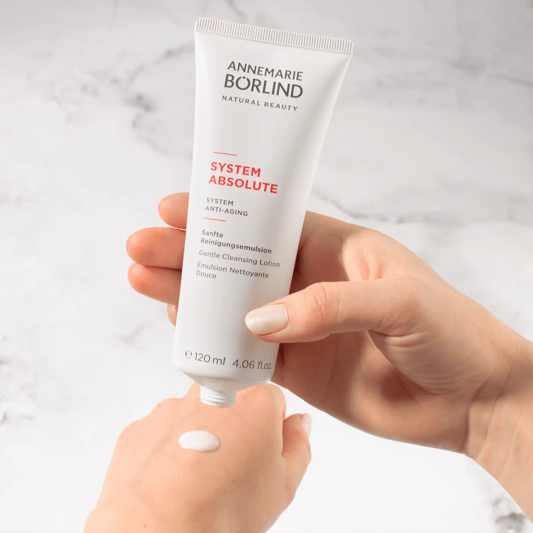 ANNEMARIE BÖRLIND SYSTEM ABSOLUTE sanfte Reinigungsemulsion in weißer Tube, Produkt auf Handrücken aufgetragen