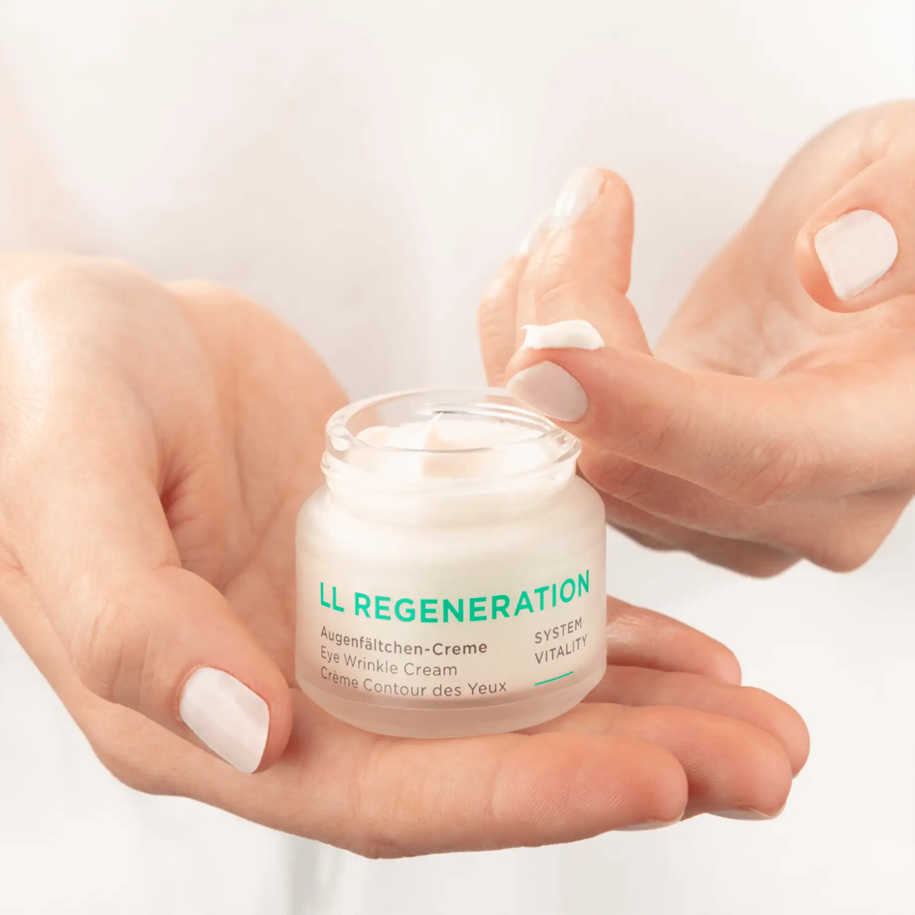 LL REGENERATION Augenfältchen-Creme im Tiegel, Creme wird mit Finger entnommen, helle Nagellacke
