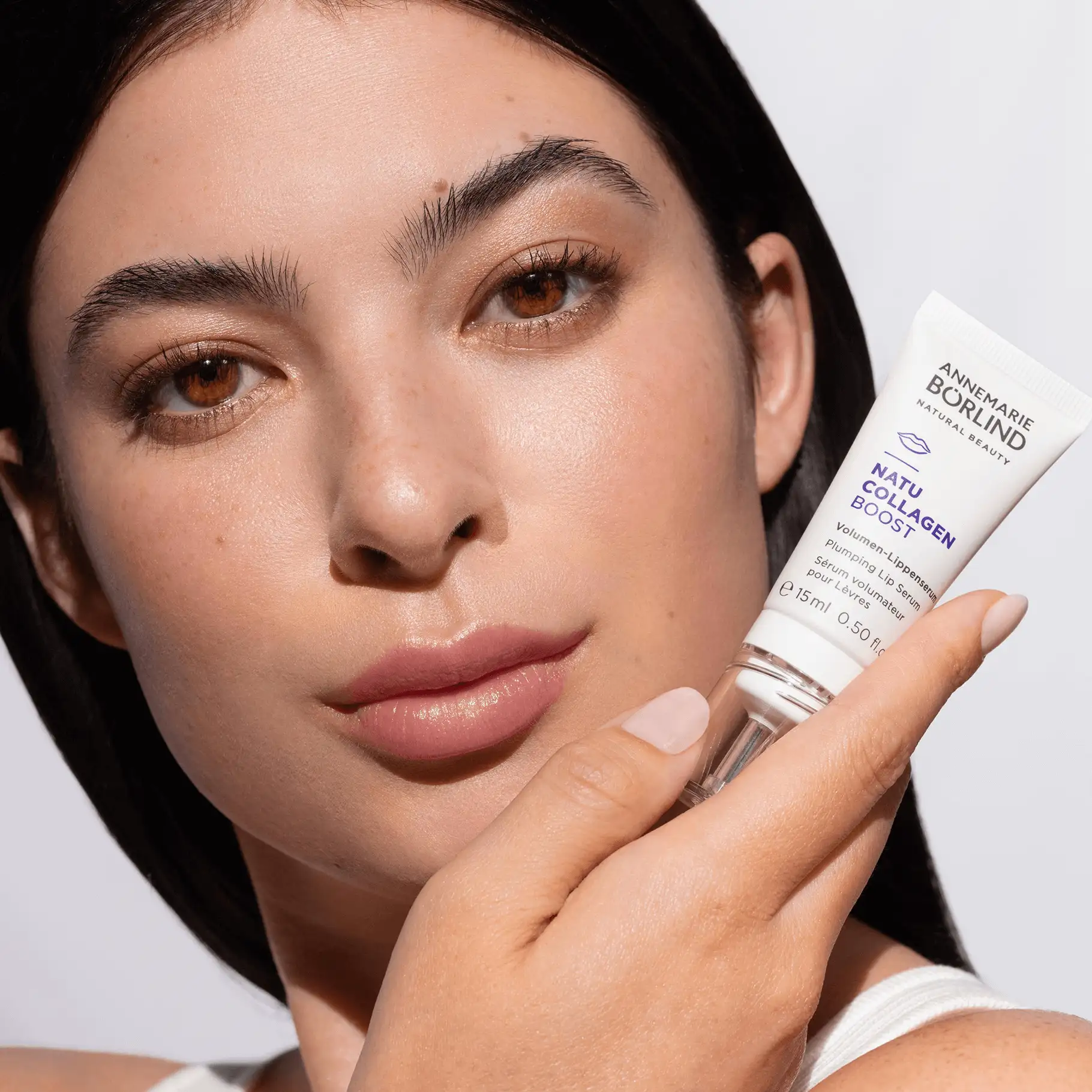 Frau hält ANNEMARIE BÖRLIND NATU COLLAGEN BOOST Volumen-Lippenserum nah an ihr Gesicht