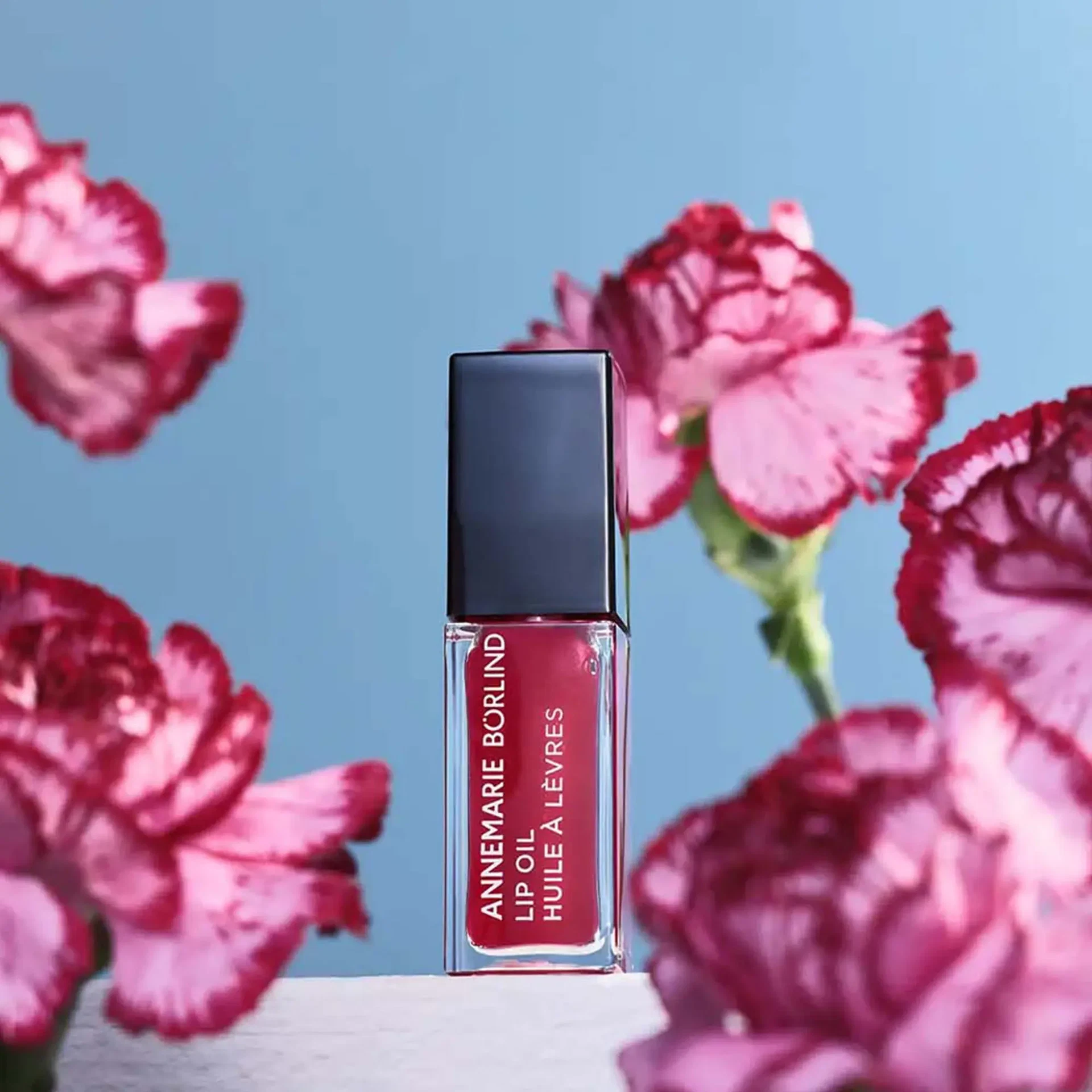 LIP OIL Wild Fuchsia von ANNEMARIE BÖRLIND vor blauem Himmel, eingerahmt von pinken Blüten