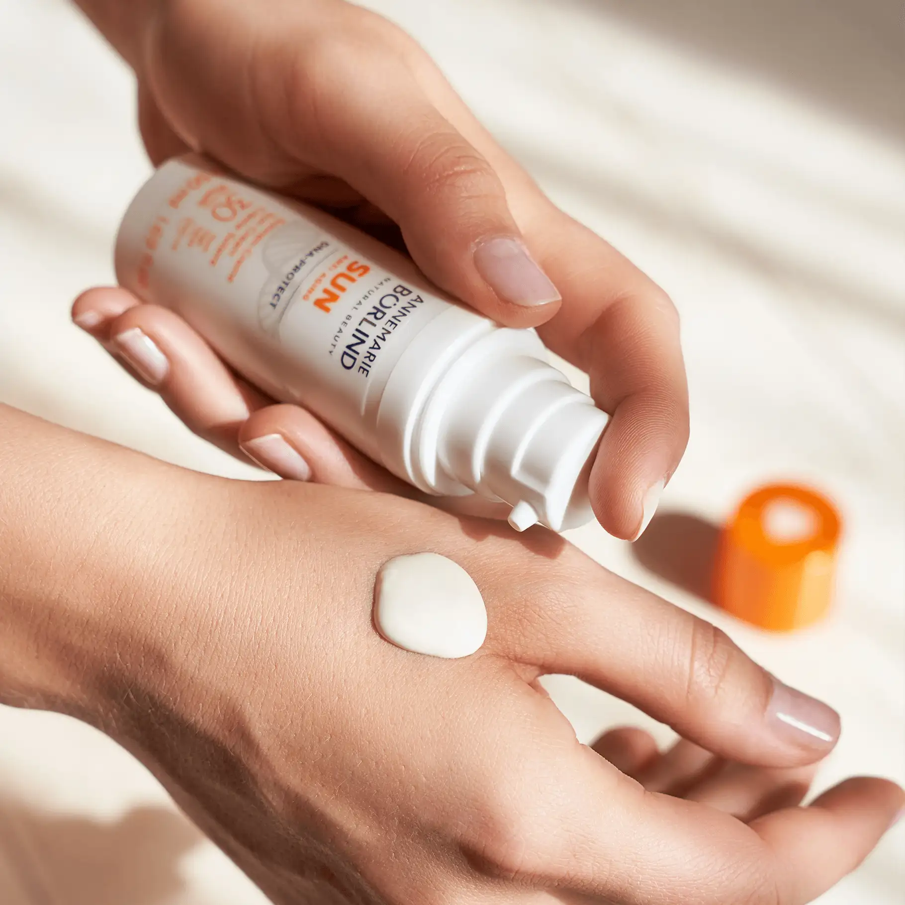 ANNEMARIE BÖRLIND SUN Anti-Aging DNA Protect LSF 30, weiße Creme auf Hand, Spenderflasche in Hand gehalten