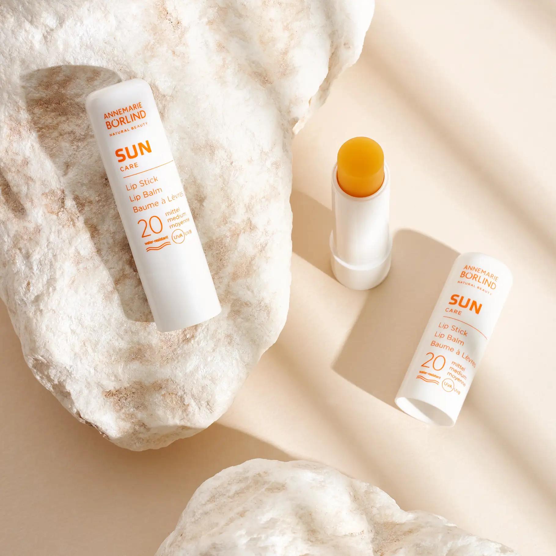 ANNEMARIE BÖRLIND SUN CARE Lip Stick mit LSF 20, zwei geschlossene und ein geöffneter Lippenpflegestift auf Steinen