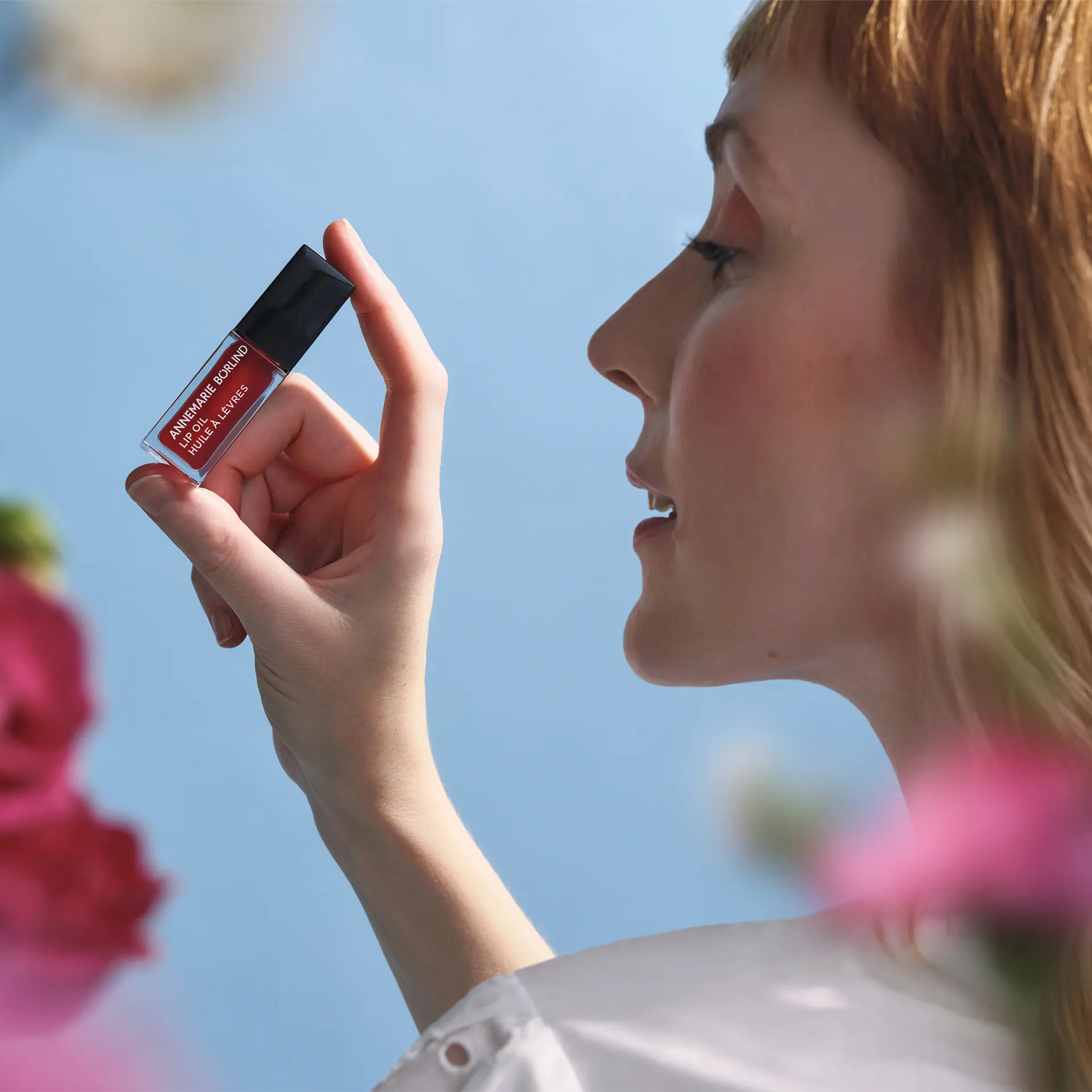 ANNEMARIE BÖRLIND Lip Oil Wild Fuchsia vor Gesicht einer Frau mit hellorangenen Haaren