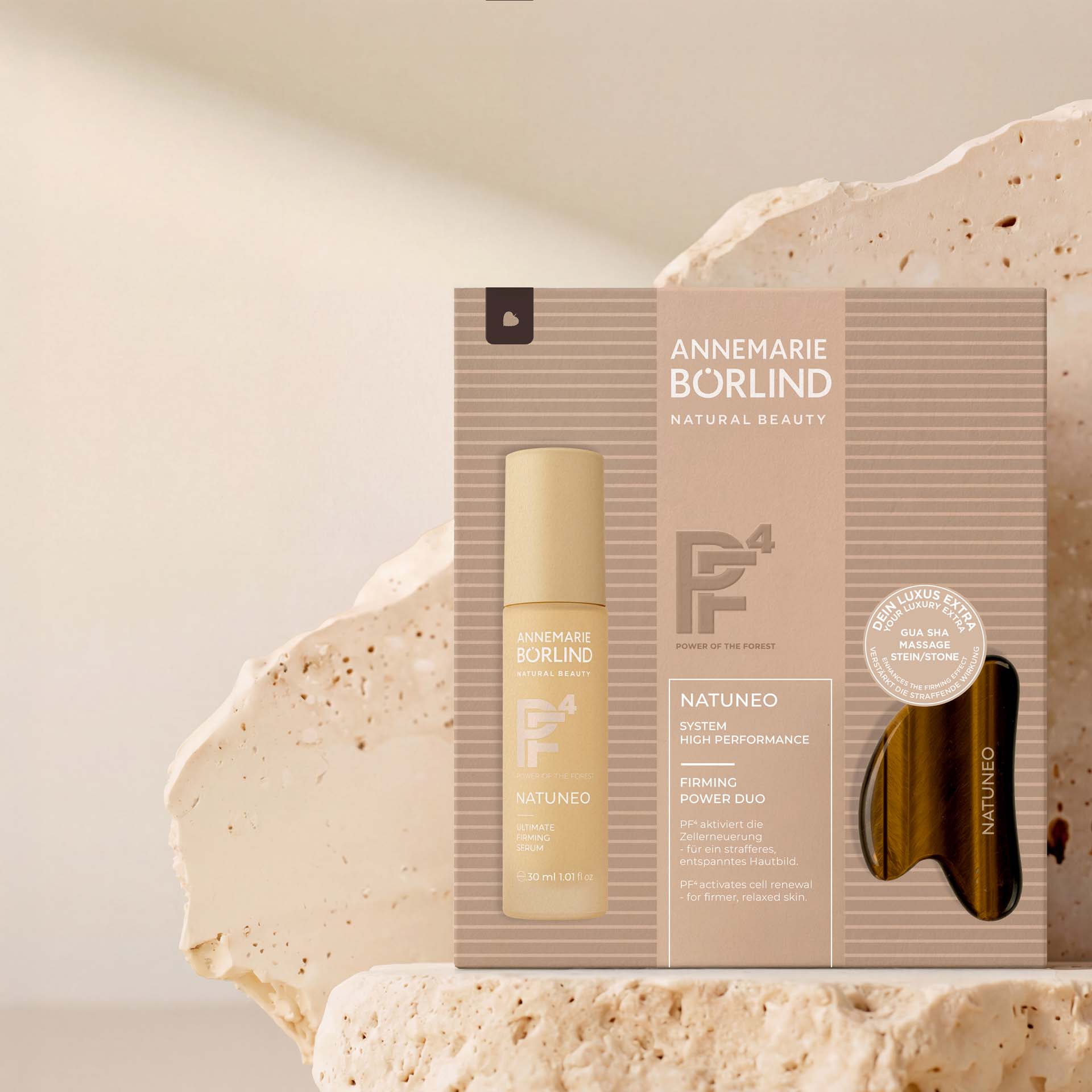 NATUNEO Firming Power Duo Faltschachtel mit Firming Serum und Gua Sha Stein vor beigem Stein im Hintergrund