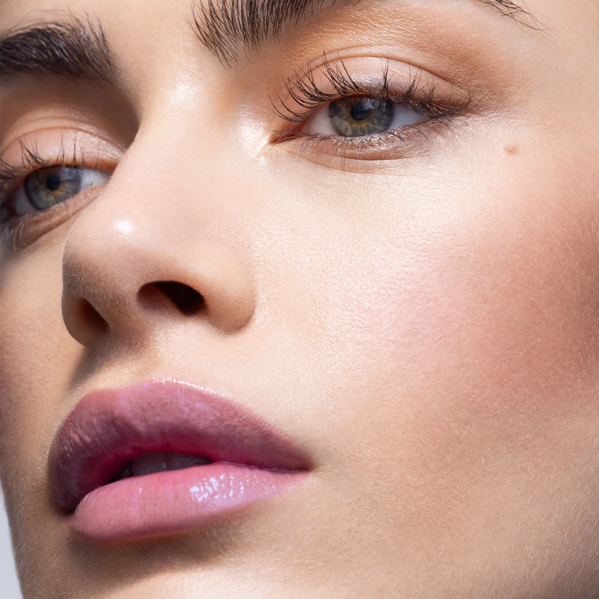 Nahaufnahme eines Gesichts mit glatter, strahlender Haut, dezent geschminkten Lippen und betonten Wimpern