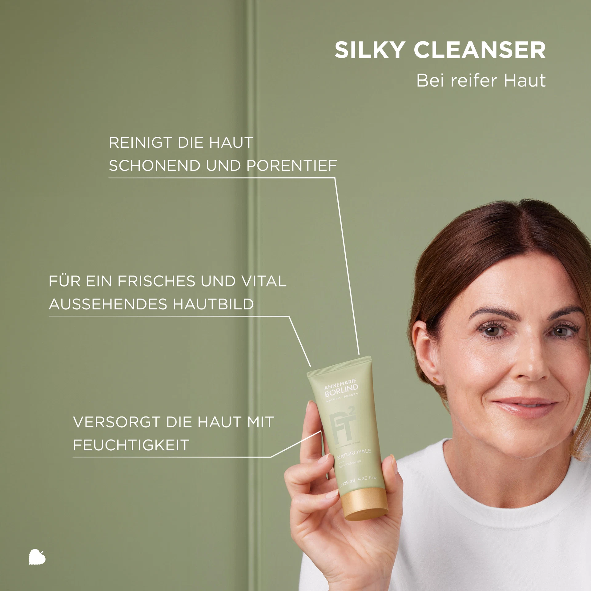 Frau hält ANNEMARIE BÖRLIND NATUROYALE Silky Cleanser für reife Haut vor grünem Hintergrund
