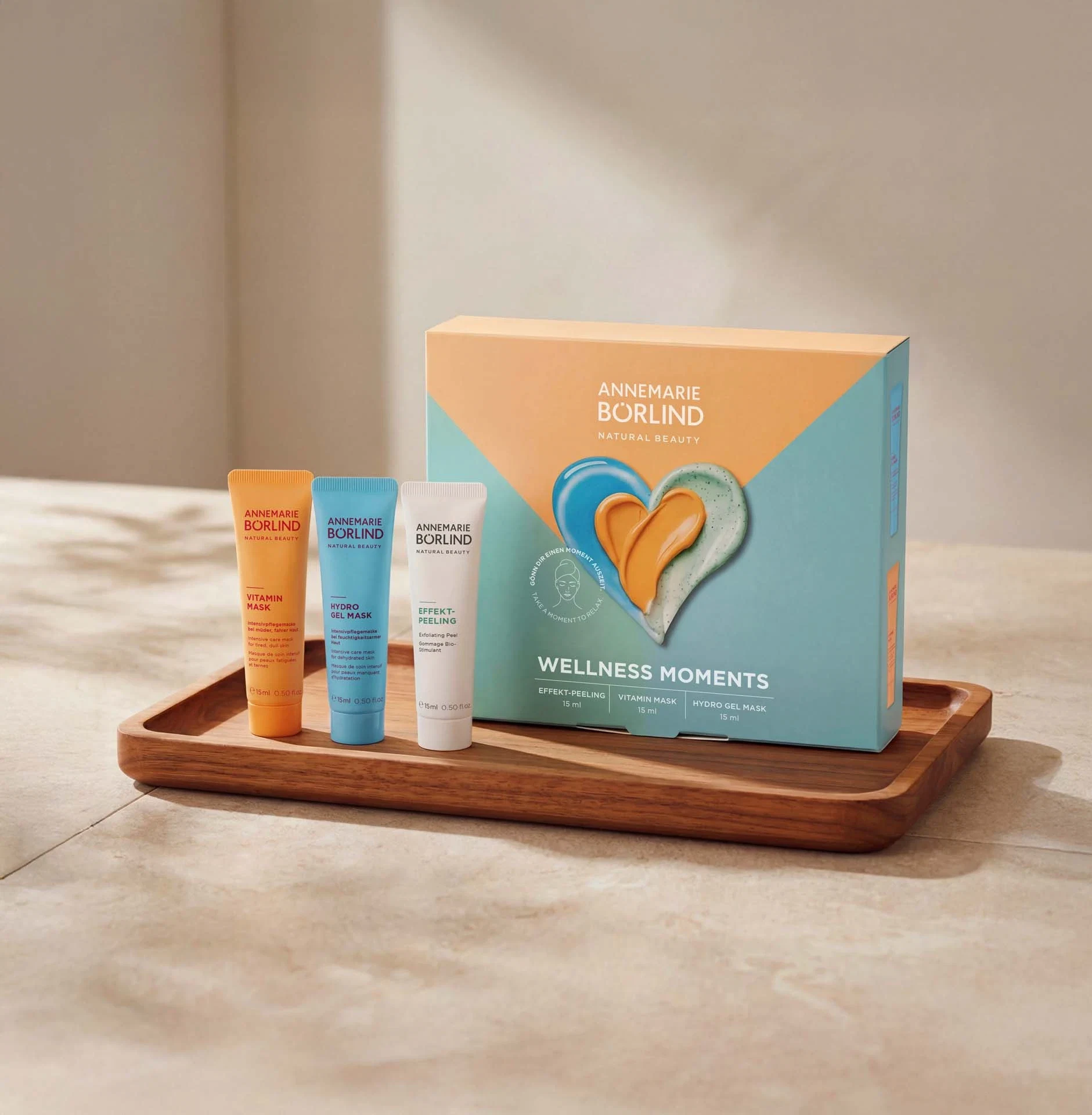 ANNEMARIE BÖRLIND Wellness Moments Set, Abbildung der Hydro Gel Mask, Vitamin Mask und Effektpeeling neben der Faltschachtel auf Holzbrett