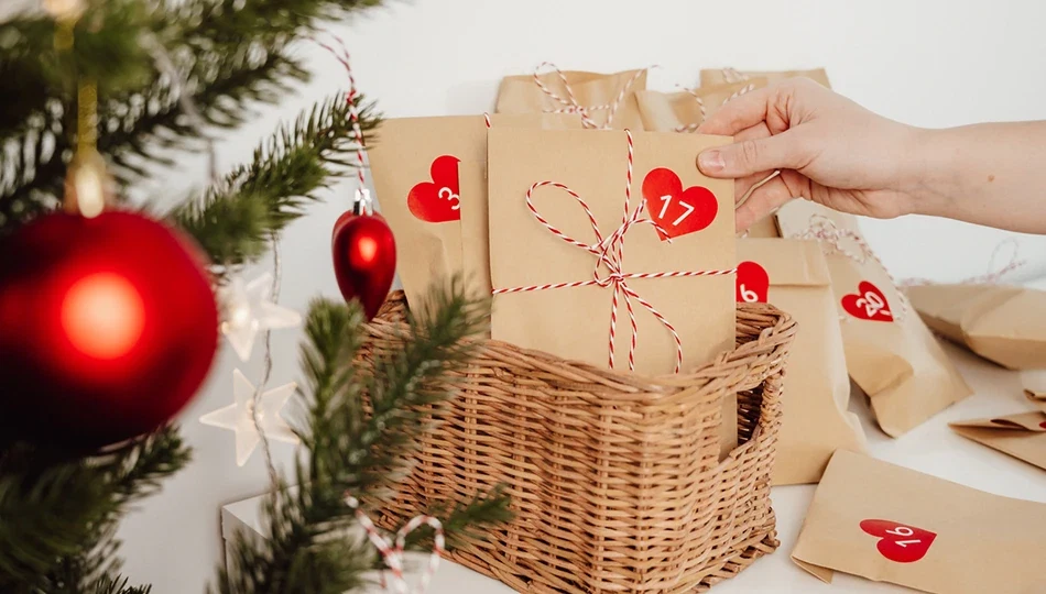 Selbstgemachter Beauty-Adventskalender mit liebevoll verpackten Papiertüten und roten Herzaufklebern neben einem geschmückten Weihnachtsbaum