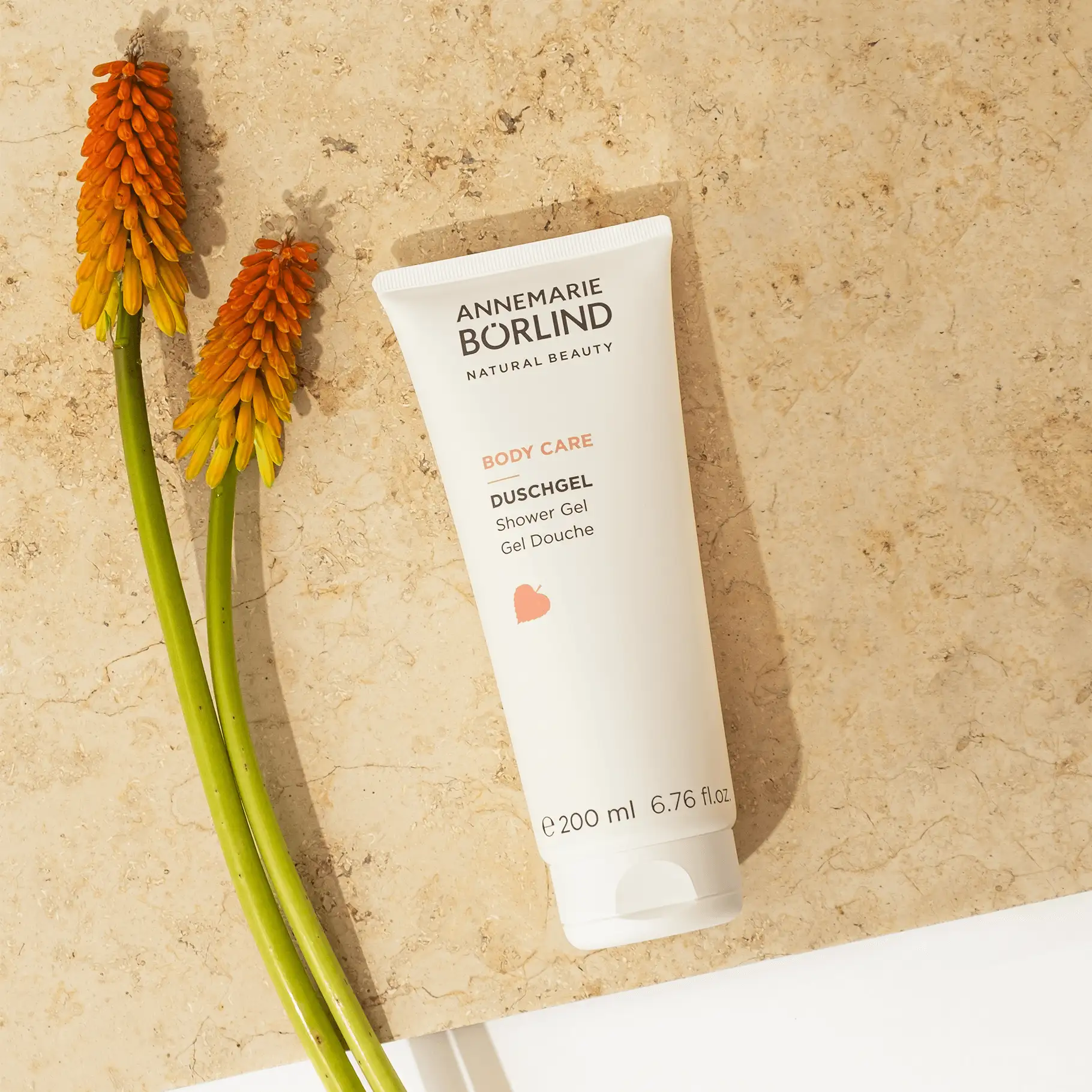 ANNEMARIE BÖRLIND Body Care Duschgel 200 ml auf Marmorplatte mit zwei orangen Blütenstielen