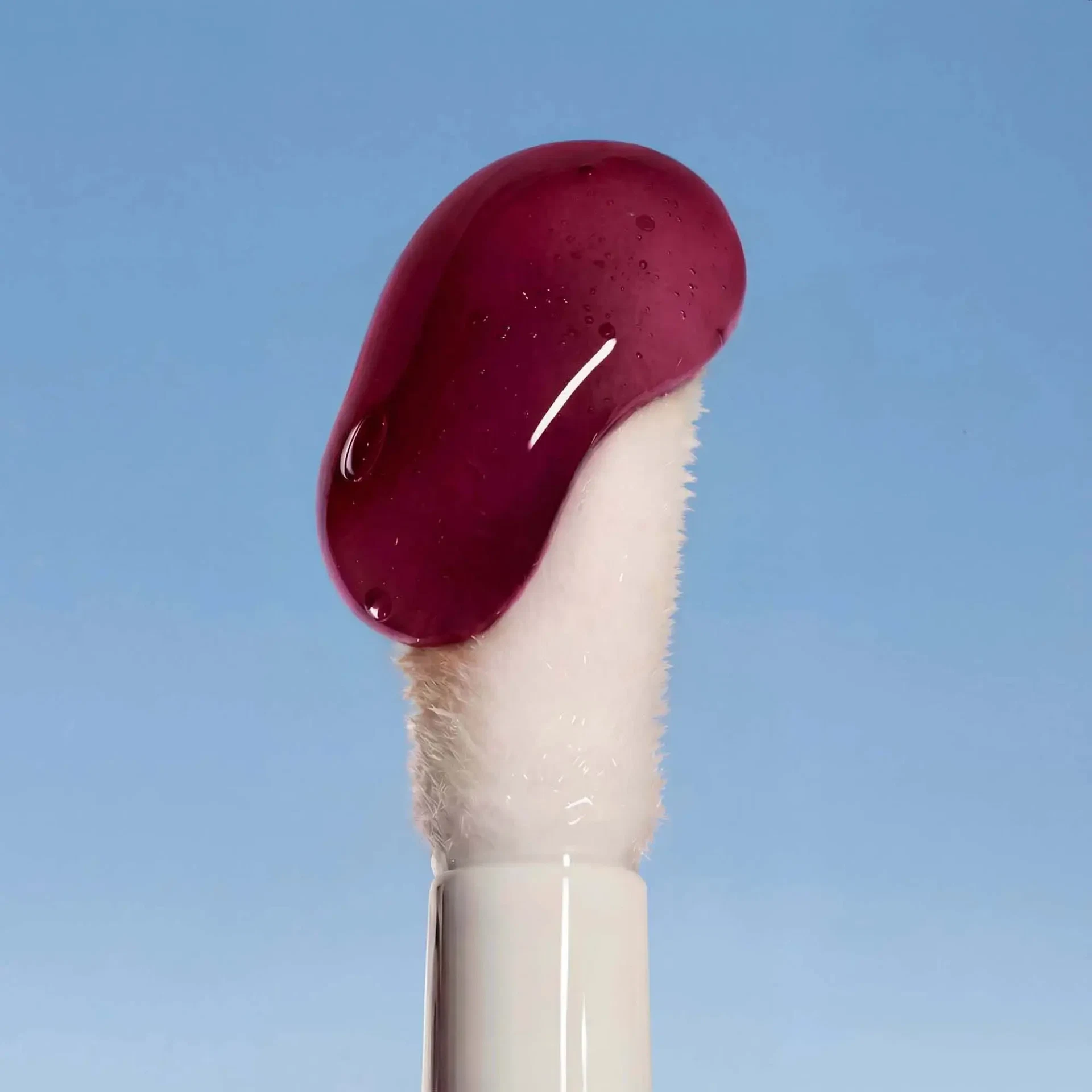 Applikator des LIP OIL Wild Fuchsia mit glänzender, kräftig pinker Textur vor blauem Hintergrund