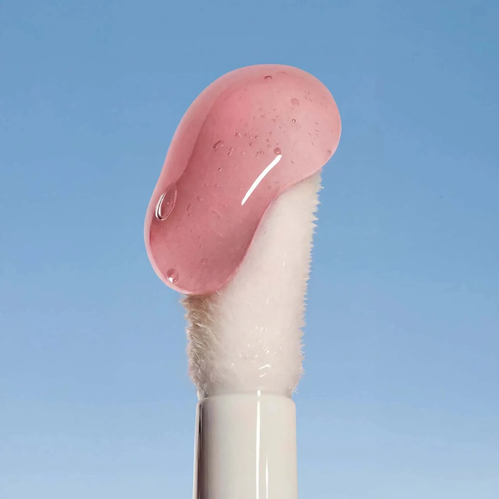 Applikator des LIP OIL Cherry Blossom mit glänzender, roséfarbener Textur vor blauem Hintergrund