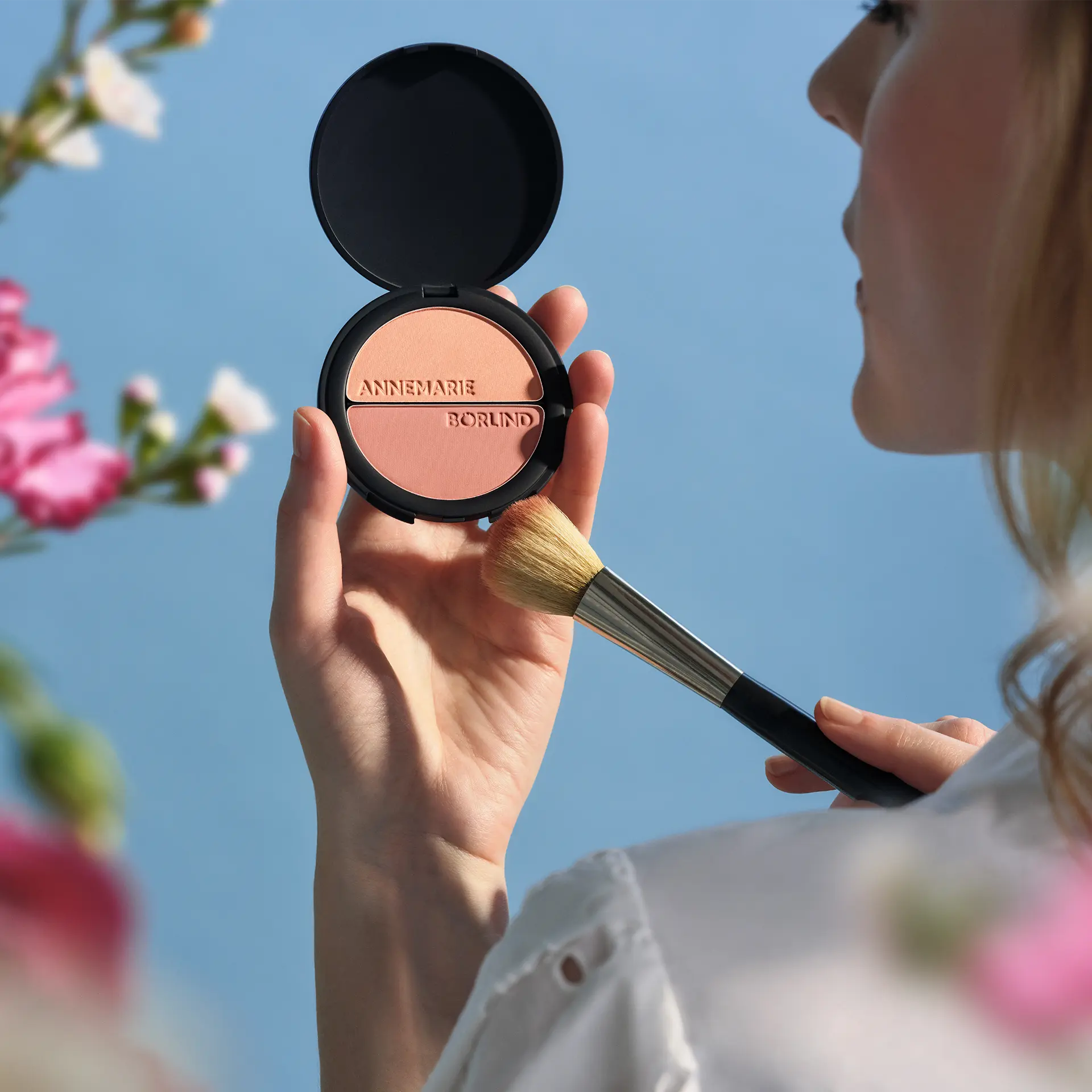 ANNEMARIE BÖRLIND Duo Blush & Eye Shadow in schwarzer Dose mit Logo in der Hand eines Models mit Pinsel