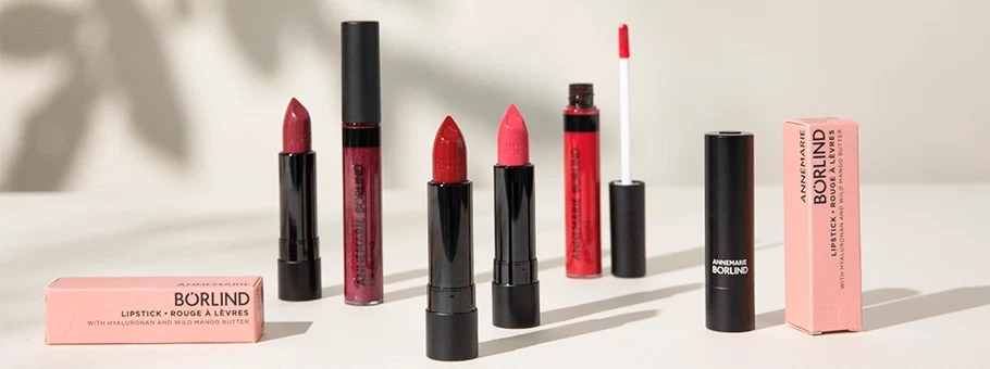 ANNEMARIE BÖRLIND Lippenstifte und Lipgloss in verschiedenen Rottönen mit Verpackungen auf hellem Untergrund
