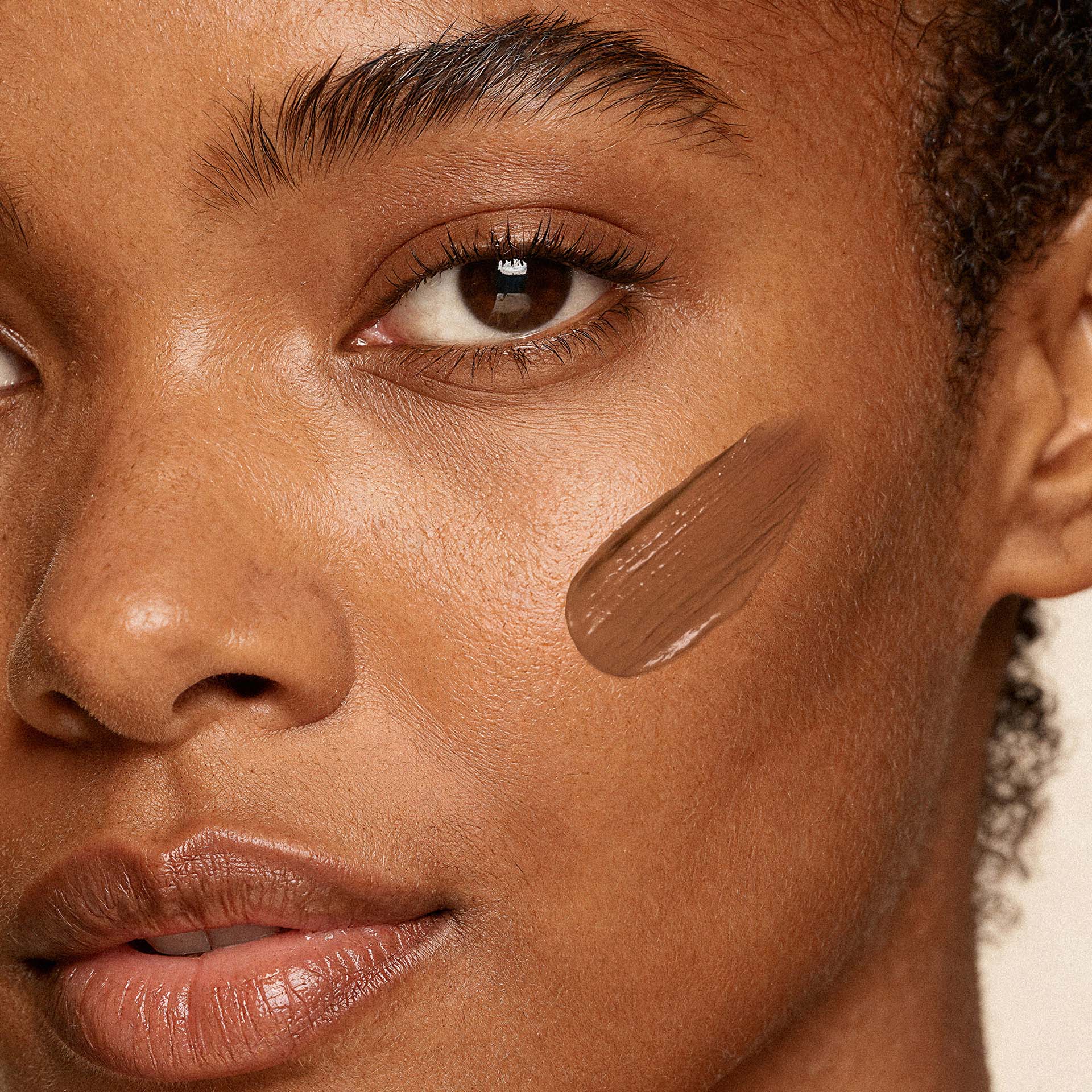 Frau mit dunklerem Teint trägt Anti-Aging Make-up in Caramel auf Wange