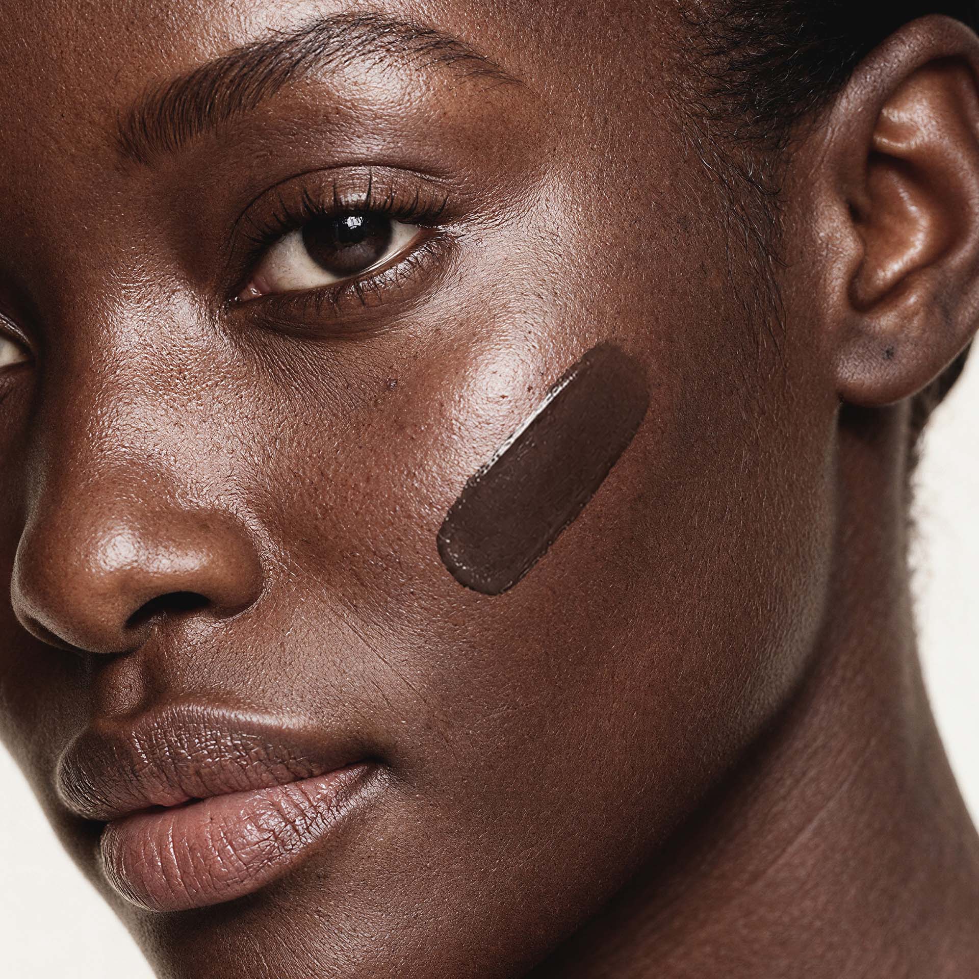 Frau mit sehr dunklem Teint trägt Anti-Aging Make-up in Dark auf Wange