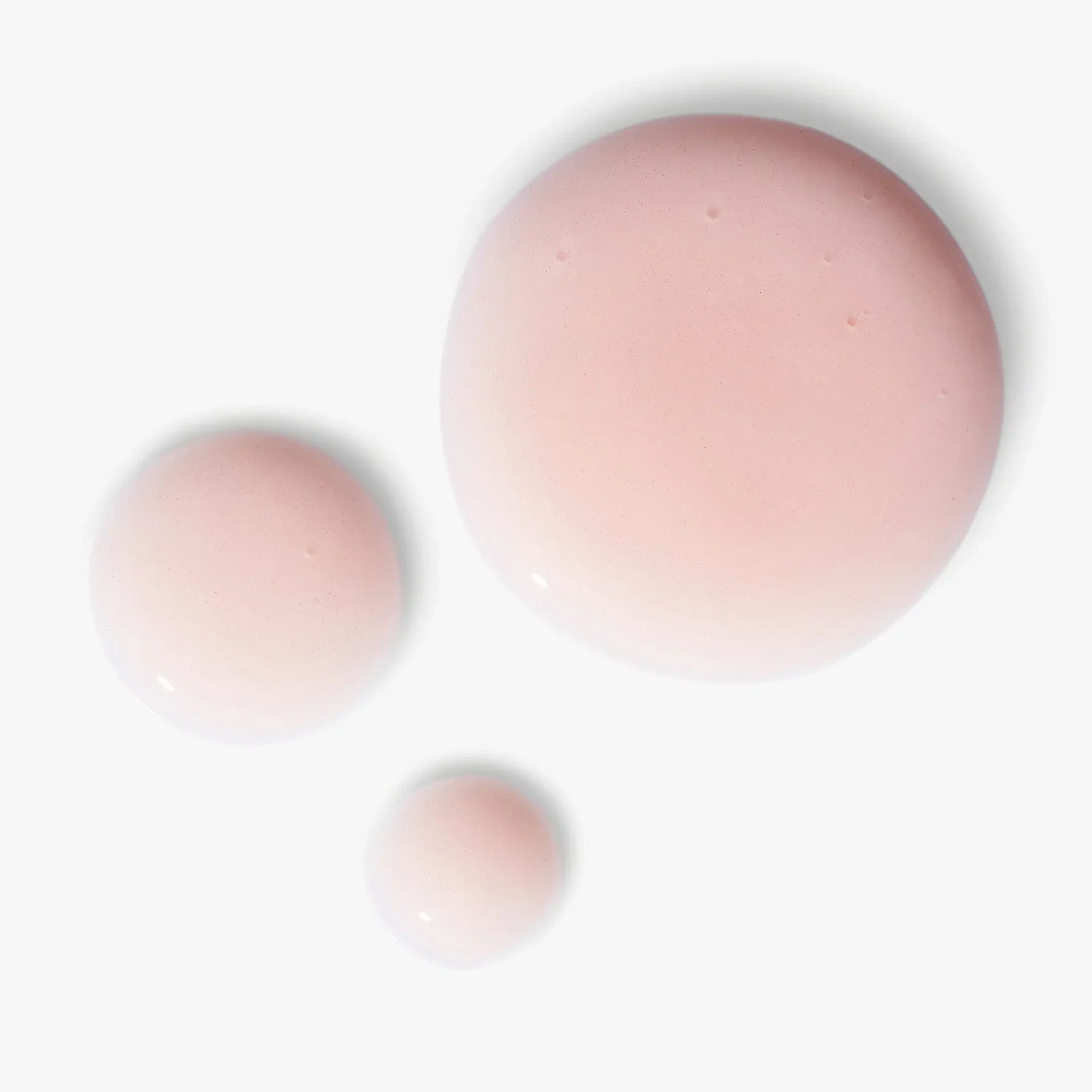 Drei Tropfen roséfarbenes NATUCOLLAGEN BOOST Augenserum auf hellem Hintergrund