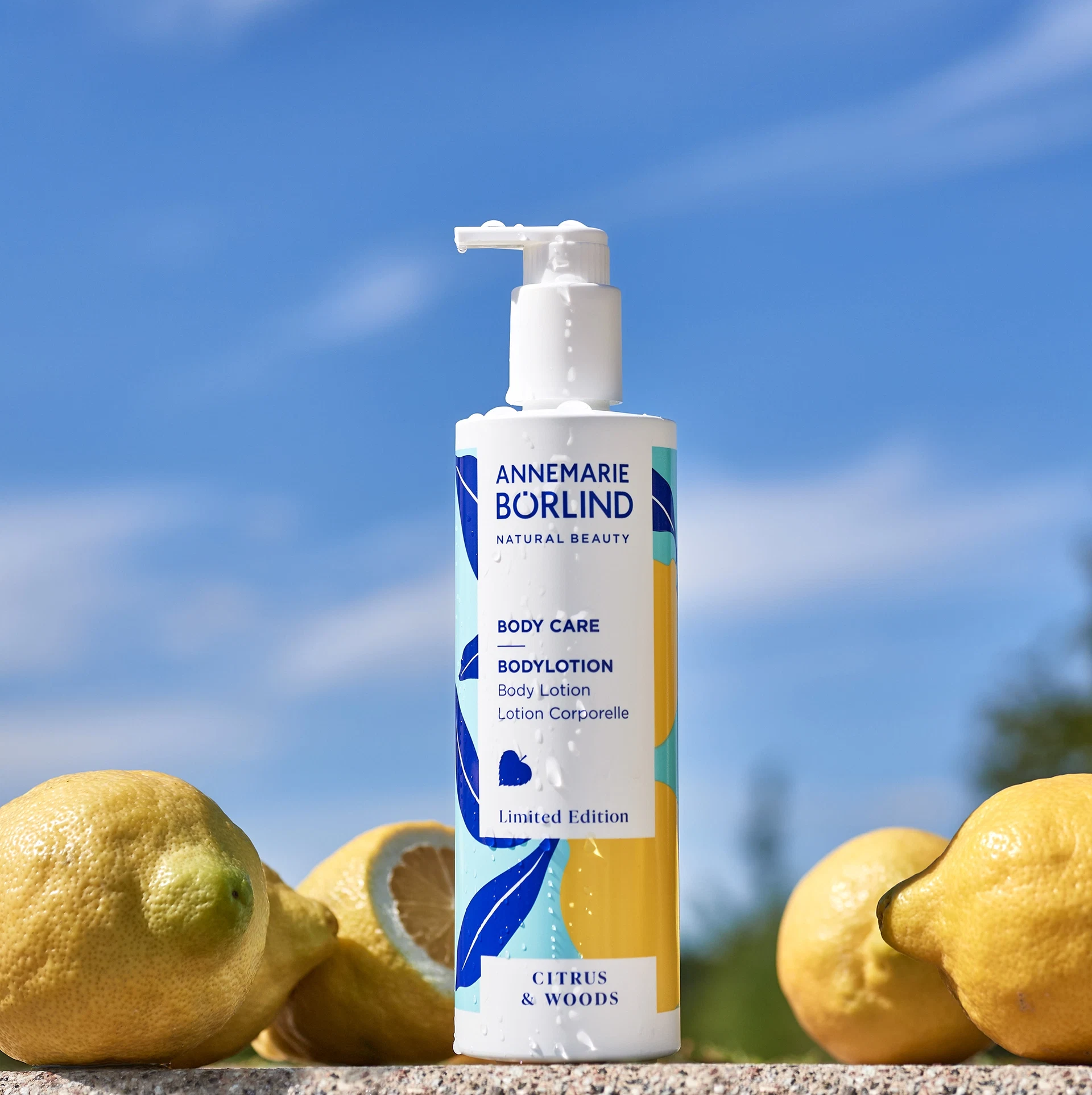 ANNEMARIE BÖRLIND Bodylotion Citrus & Woods mit Pumpspender, umgeben von frischen Zitronen vor blauem Himmel