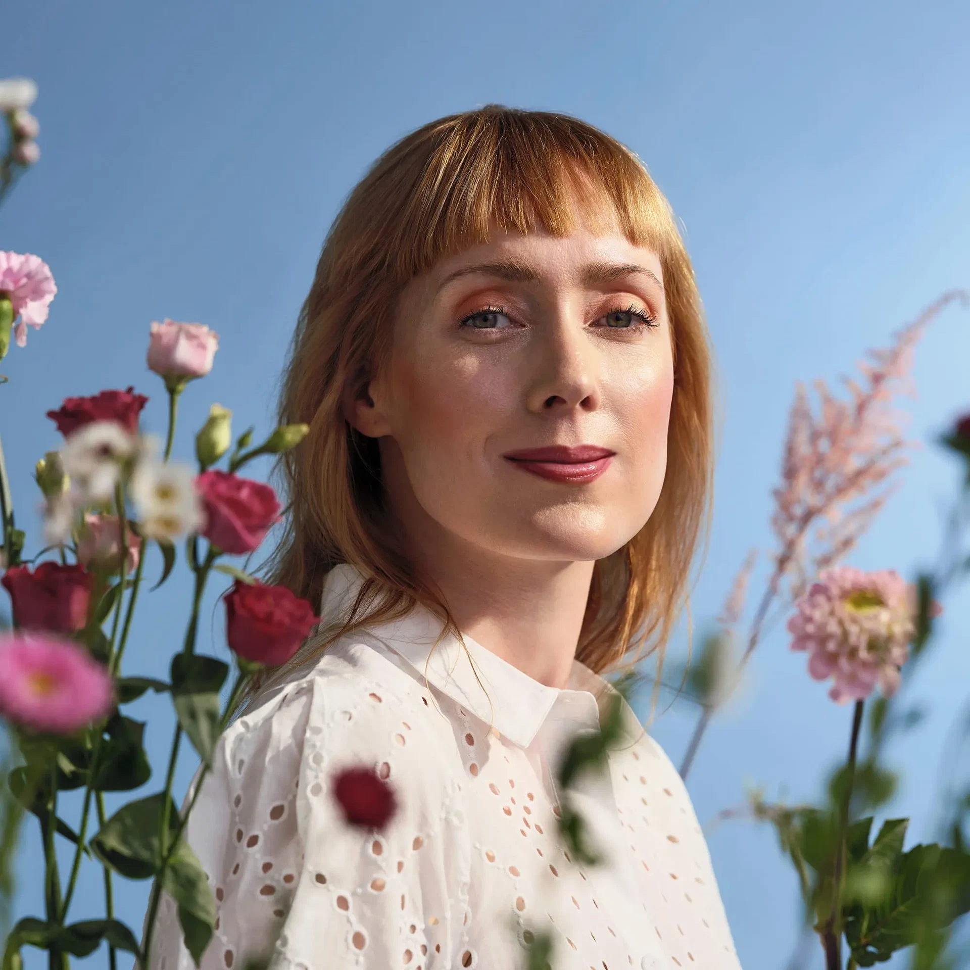 Model mit Season of Bloom Make-up-Look zwischen rosa und pinken Blüten vor blauem Hintergrund