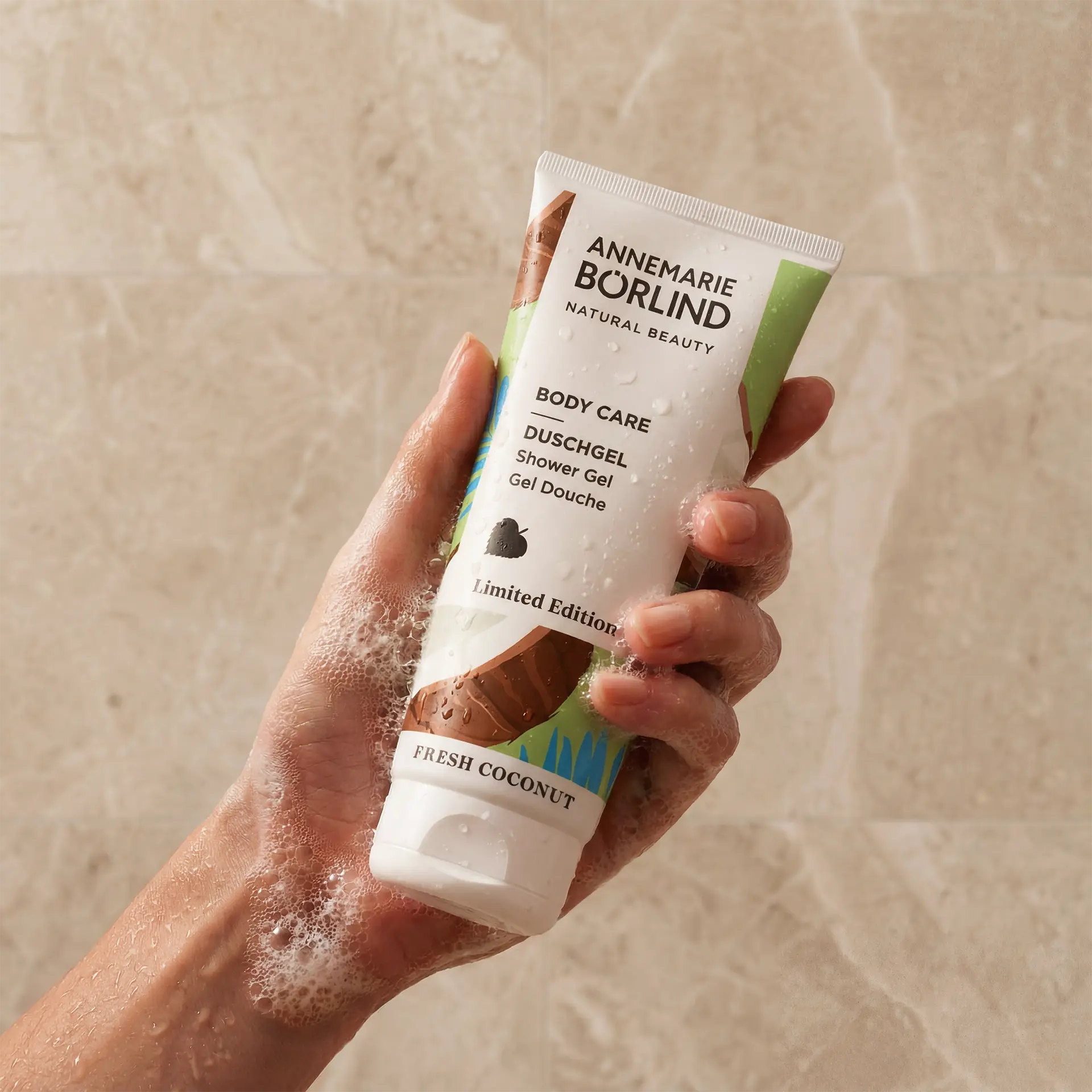 BODY CARE Duschgel Fresh Coconut in Tube mit sommerlichem Design in Hand vor beigem Hintergrund
